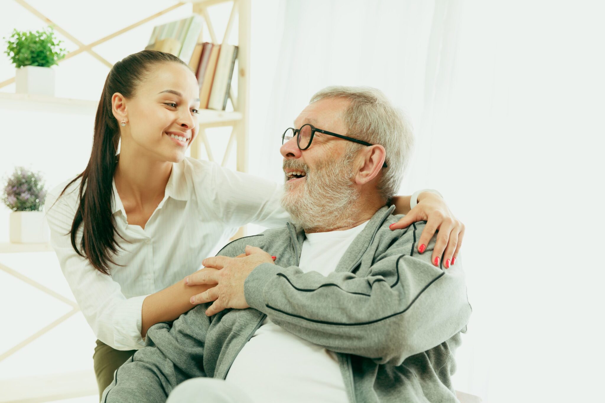 A daughter or granddaughter spends time with the grandfather A daughter or granddaughter spends time with the grandfather or senior man. Family or fathers' day, positive emotions and happieness. Lifestyle portrait at home. Two people caddling and smiling.