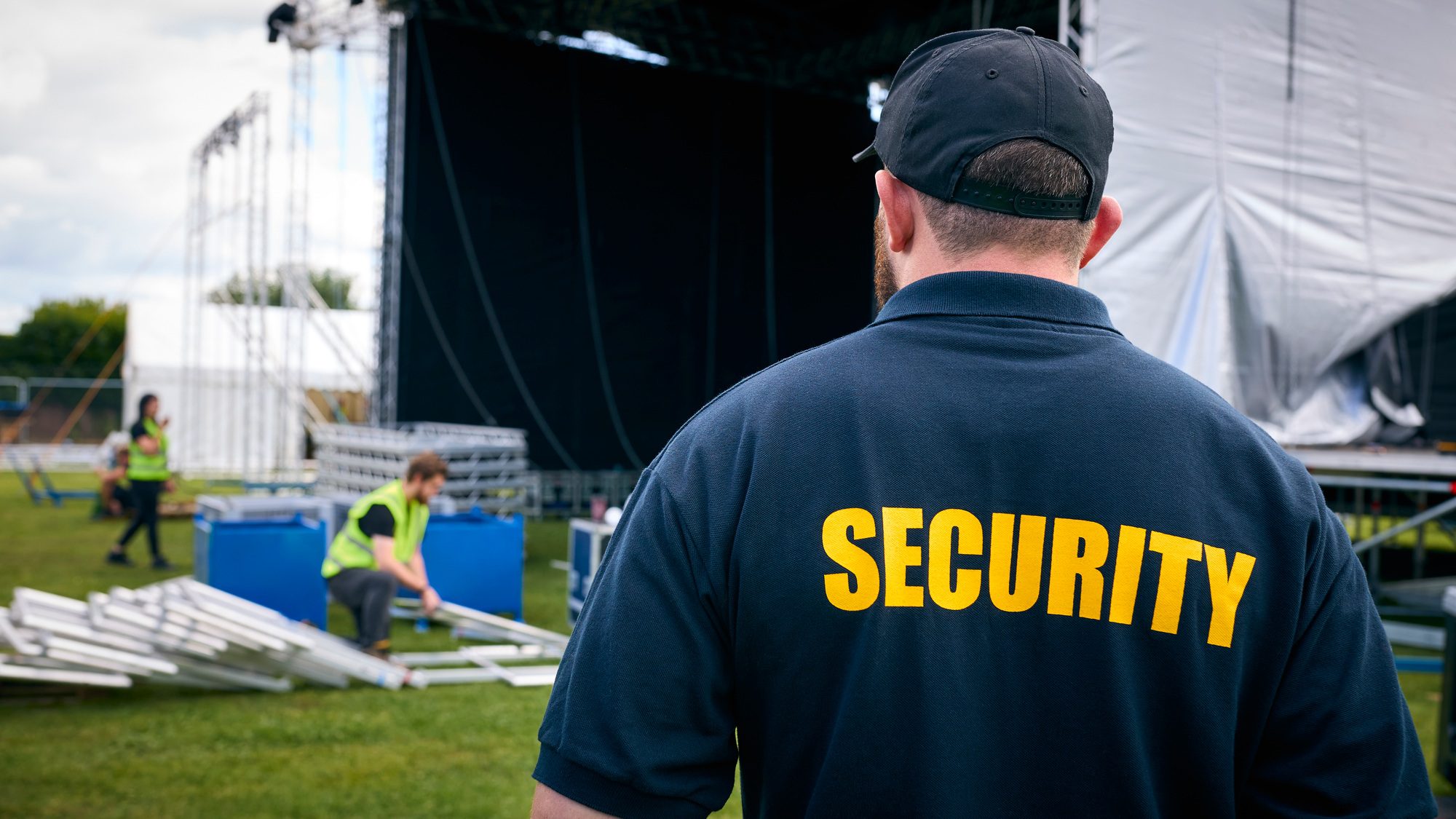 Rear View Of Security Team At Outdoor Stage For Music Festival Or Concert Rear View Of Security Team At Outdoor Stage For Music Festival Or Concert